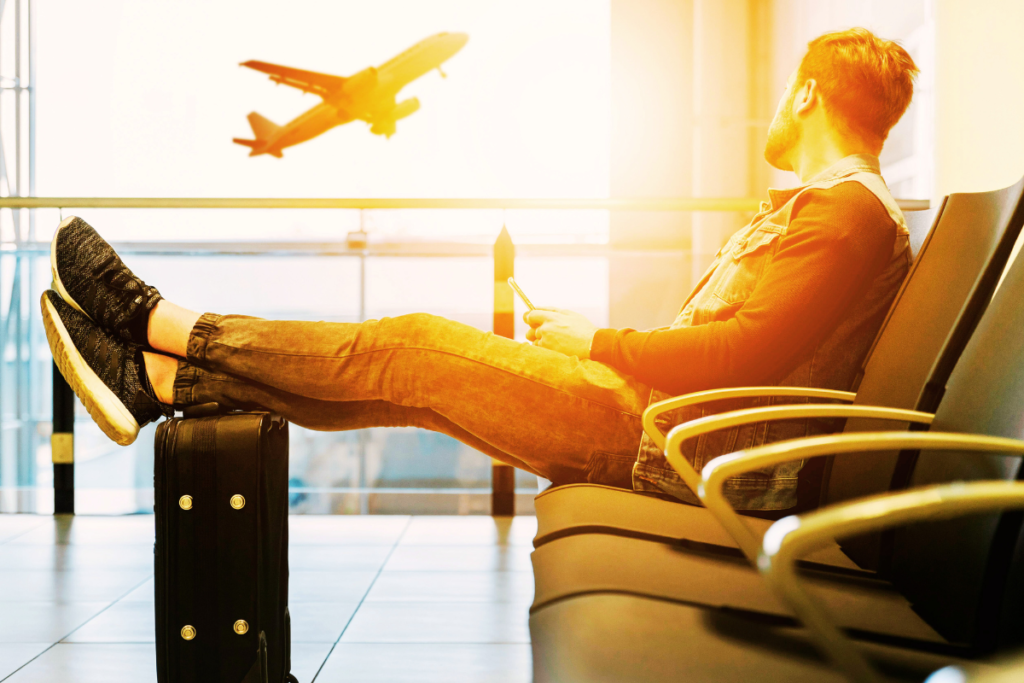 Traveler relaxing in an airport lounge with sunlight streaming through the windows and a plane visible in the background.